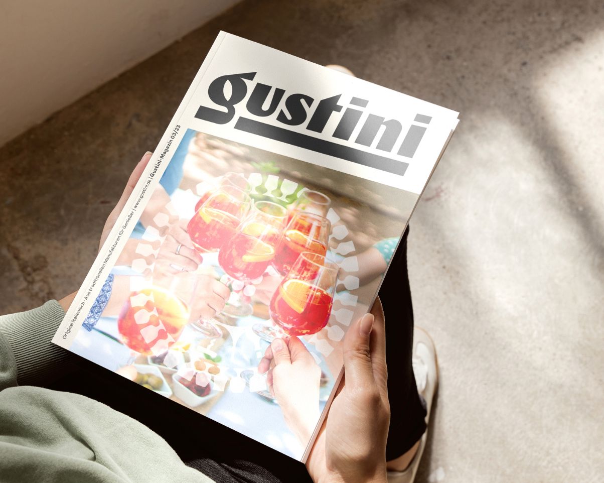 eine junge Person hält das Gusto-Magazin der Gustini GmbH in den Händen, auf dem Cover sind anstoßende Gläser mit Aperol Spritz zu sehen